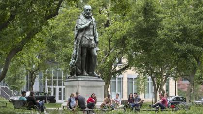 Students pass time talking and reading their cell phones at the base of Silent Willie sculpture