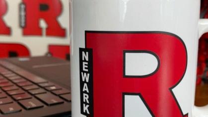 A block R coffee mug sits by a computer