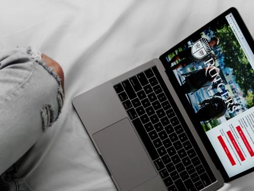 Someone sitting on a bed with an open laptop