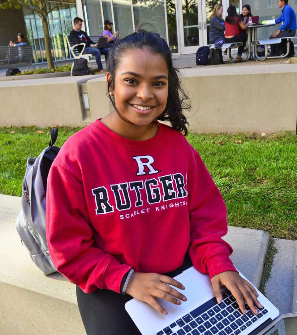 A young student works on a laptop while sitting outside